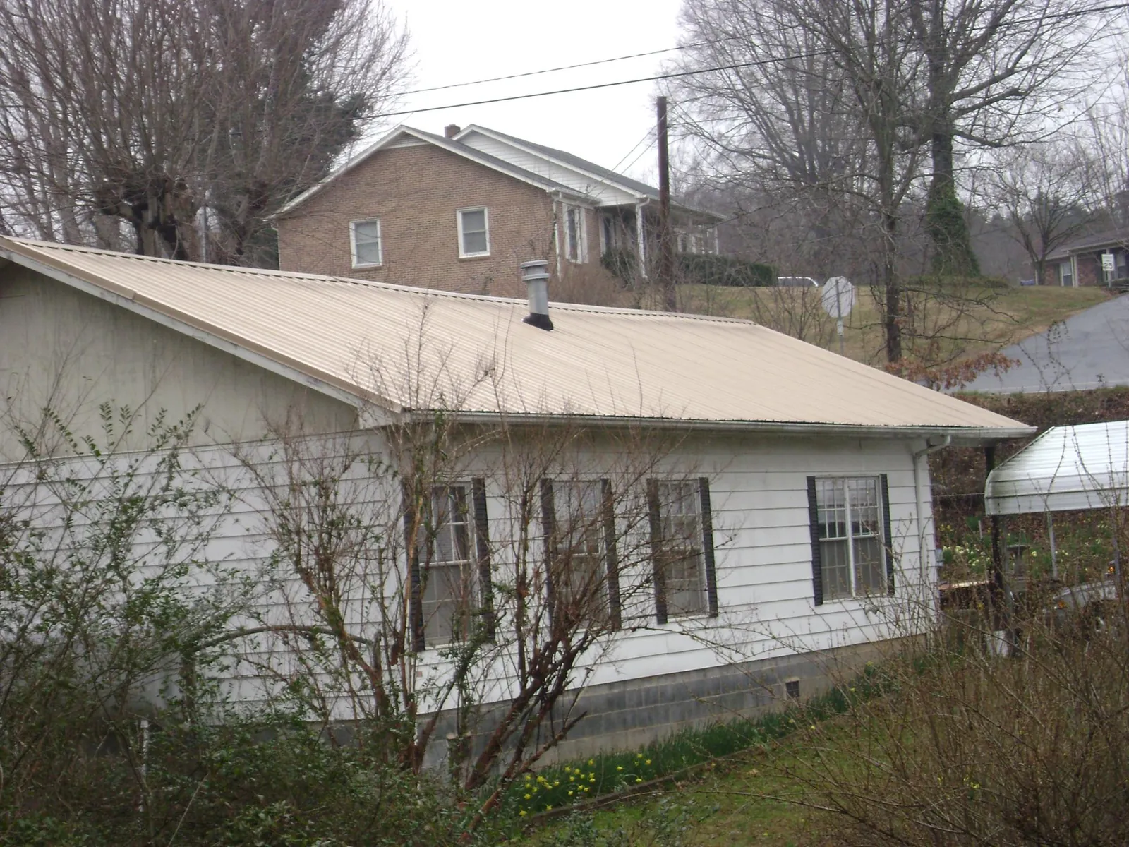 Tan metal roof on a white sided house set into a hillside — Commercial Roofing by Roofing Brothers in Albion